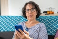 Cheerful brunette senior woman using smartphone while sitting on sofa