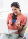 Cheerful brunette sitting on her sofa using laptop to shop online Royalty Free Stock Photo