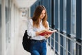 Cheerful brunette student girl with black backpack holds books in modern building. female student standing with books in college