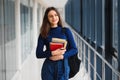 Cheerful brunette student girl with black backpack holds books in modern building. female student standing with books in college