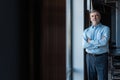 Cheerful businessman with arms folded looking at the camera while standing near the window in office building. Royalty Free Stock Photo