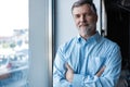 Cheerful businessman with arms folded looking at the camera while standing near the window in office building. Royalty Free Stock Photo