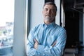 Cheerful businessman with arms folded looking at the camera while standing near the window in office building. Royalty Free Stock Photo