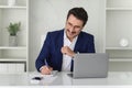 Cheerful businessman in a blue suit punches the air with joy while working on his laptop at a white desk Royalty Free Stock Photo