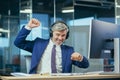 Businessman on a break listening to music and dancing with big headphones, senior and experienced gray-haired man working Royalty Free Stock Photo