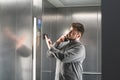 Cheerful businessman explaining something by the phone in the elevator, wearing shirt. Young man employee is expressive talking on