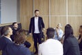 Cheerful businessman standing talking to colleagues who are sitting in circle around him in office. Royalty Free Stock Photo