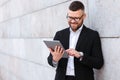 Cheerful businessman in suit using digital tablet while standing outside against concrete wall Royalty Free Stock Photo