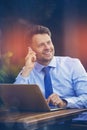 Cheerful businessman talking on mobile phone while using laptop Royalty Free Stock Photo