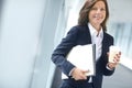 Cheerful businesswoman holding folders and drinking a coffee at work. One female businessperson carrying files and