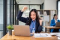 A cheerful businesswoman is receiving good news online, raising her hands and showing her fists Royalty Free Stock Photo