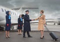 Cheerful businesswoman shaking hands aviator near plane