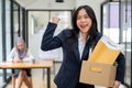 A cheerful businesswoman is showing her fist and carrying a cardboard box, happy to quit her job Royalty Free Stock Photo