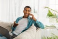 Cheerful busy millennial african american businessman with laptop making phone call on sofa in living room