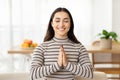 Cheerful calm young arab woman meditates with closed eyes on sofa, make pray sign Royalty Free Stock Photo