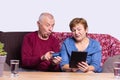 Cheerful caucasian grey senior couple purchasing new furniture online, using credit card and digital tablet, just moved Royalty Free Stock Photo