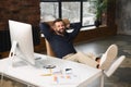Cheerful caucasian man wearing casual wear sitting at the armchair with his legs at the table and using laptop at modern Royalty Free Stock Photo