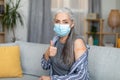 Cheerful caucasian old gray-haired woman in protective mask shows her shoulder with band-aid and thumb up Royalty Free Stock Photo