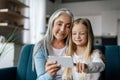 Cheerful caucasian small granddaughter and aged grandma watch video, have online call on phone, use new app