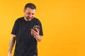 Cheerful caucasian tattooed gangster-looking guy looking at his phone and smiling. Medium studio shot. Copy space.