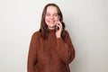 Cheerful Caucasian woman wearing brown jumper talking on mobile phone enjoying pleasant conversation looking smiling at camera Royalty Free Stock Photo