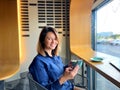 Cheerful Caucasian young beautiful lady sitting in cafeteria with cup of coffee and smartphone in hands smiling while Royalty Free Stock Photo