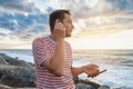 Cheerful Caucasian young man with smartphone wearing earphones on the sea coast and listening to music. Handsome male Royalty Free Stock Photo