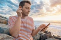 Cheerful Caucasian young man with smartphone wearing earphones on the sea coast and listening to music. Handsome male Royalty Free Stock Photo