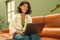 Cheerful caucasian young woman looking at camera working on laptop sitting on sofa in cafe. Royalty Free Stock Photo