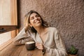 Cheerful caucasian young woman smiling, eyes closed, sitting indoors with coffee. Royalty Free Stock Photo