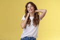 Cheerful charismatic good-looking curly-haired woman stretching posing yellow background touch neck flirty smiling