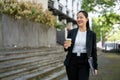 A cheerful businesswoman with a takeaway coffee cup and binders in her hands is walking in the city Royalty Free Stock Photo