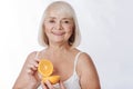 Cheerful charming woman using orange halves in cosmetics