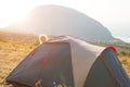 Cheerful child looks out from behind a tourist tent in the mountains with a panoramic view at dawn. Domestic tourism, active
