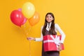 cheerful child with party helium balloons and present box on yellow background