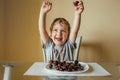 The cheerful child raised his hands up and rejoiced in the cherries in the plate. he sits in the kitchen