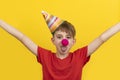 Cheerful child with red clown nose and festive hat on yellow background. April fools day Royalty Free Stock Photo