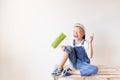 A cheerful child sits on a construction ladder in an apartment with white walls and a roller in his hands and shows a thumbs up, a Royalty Free Stock Photo