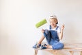 A cheerful child sits on a construction ladder in an apartment with white walls and a roller in his hands and shows a thumbs up, a Royalty Free Stock Photo