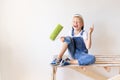 A cheerful child sits on a construction ladder in an apartment with white walls and a roller in his hands and shows a thumbs up, a Royalty Free Stock Photo