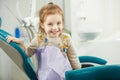 Cheerful child sits in dentist chair with napkin on chest