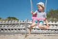 A cheerful child swings on the beach as he looks into the distance. A sunny summer day, blue skies and a happy childhood