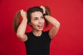 Cheerful childish woman 20s in black t-shirt having fun and making two ponytails with her brown hair, isolated over red background Royalty Free Stock Photo