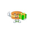 Cheerful chocolate macarons cartoon character holding a gift box Royalty Free Stock Photo