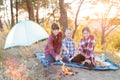 A cheerful company of two girls and a boy on a picnic in the middle of the forest. Children fry sausages on the fire, eat buns and