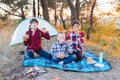 A cheerful company of two girls and a boy on a picnic in the middle of the forest. Children fry sausages on the fire, eat buns and