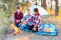 A cheerful company of two girls and a boy on a picnic in the middle of the forest. Children fry sausages on the fire, eat buns and