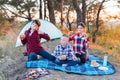 A cheerful company of two girls and a boy on a picnic in the middle of the forest. Children fry sausages on the fire, eat buns and