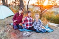 A cheerful company of two girls and a boy on a picnic in the middle of the forest. Children fry sausages on the fire, eat buns and