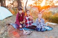 A cheerful company of two girls and a boy on a picnic in the middle of the forest. Children fry sausages on the fire, eat buns and